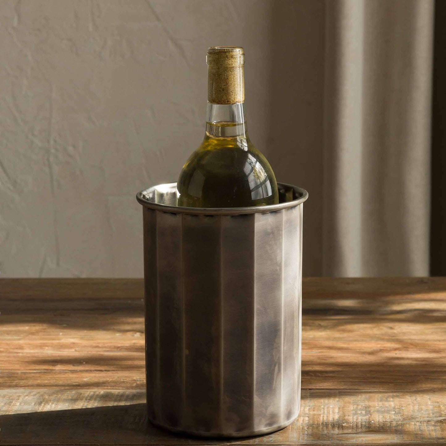 Wine bottle in a metal cooler on a wooden table with a neutral background