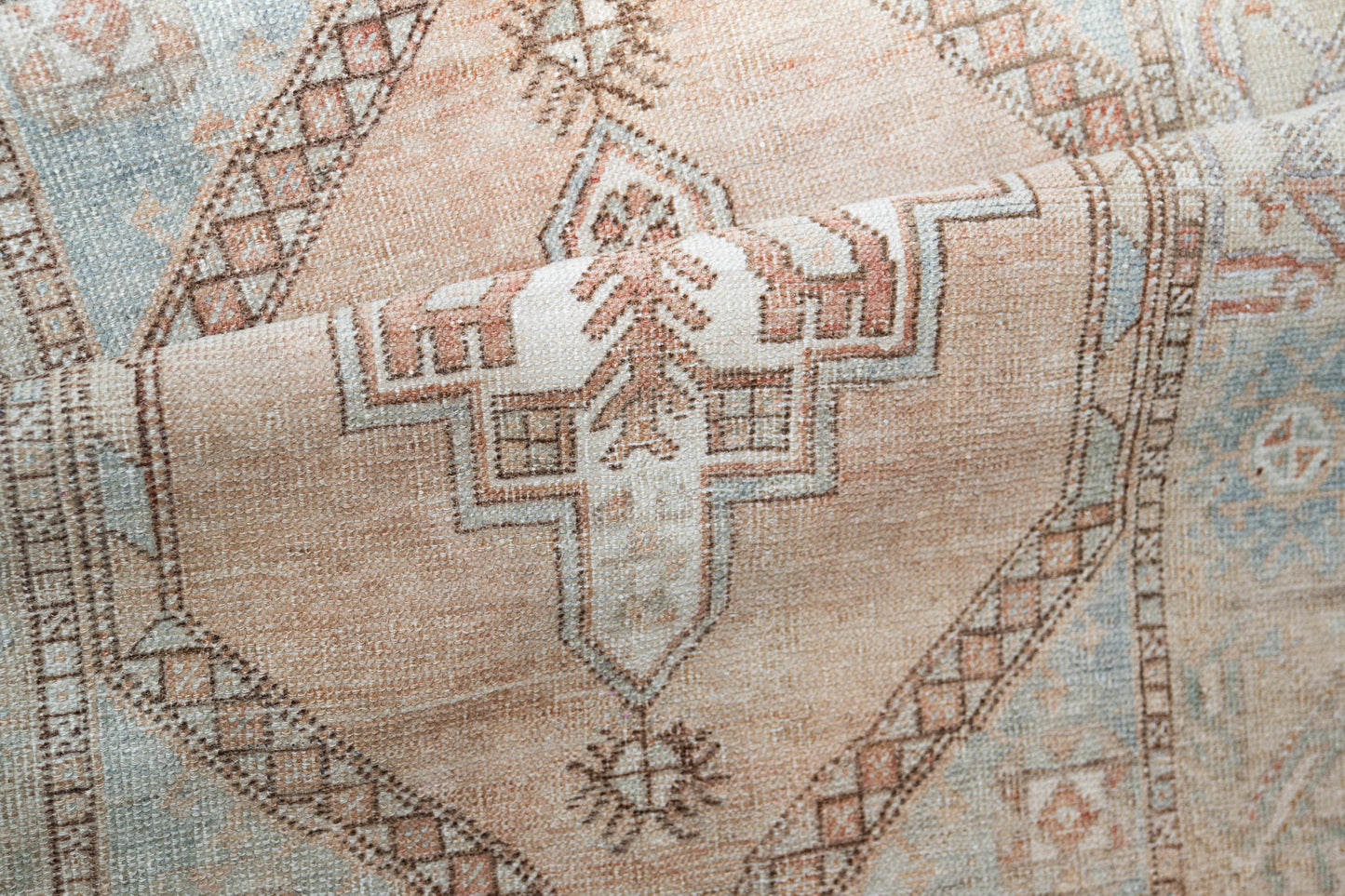 Close-up of a vintage-style geometric rug featuring a central diamond medallion in beige, dusty blue, and terracotta brown.